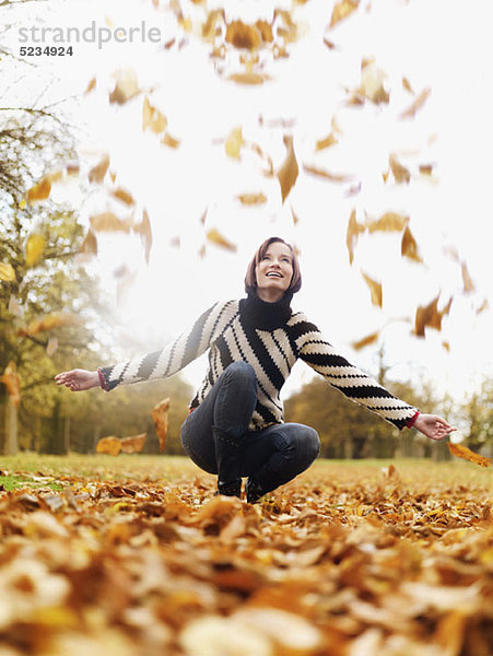 Eine Frau  die aufschaut  wenn das Herbstlaub fällt.