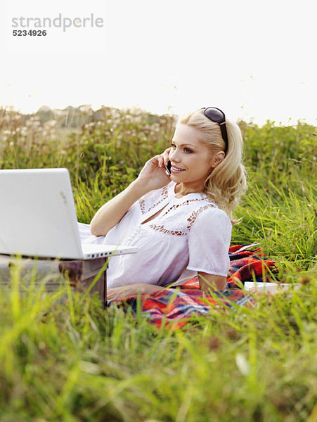 Eine Frau in der Natur mit offenem Laptop und Handy