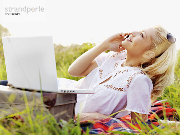 Eine Frau in der Natur mit offenem Laptop und Handy