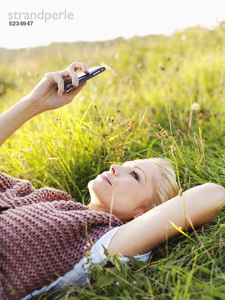 Eine Frau  die im Gras liegt und ihr Smartphone ansieht.