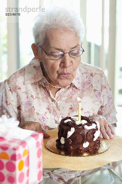 Eine ältere Frau  die eine Kerze auf einem Geburtstagskuchen ausbläst.