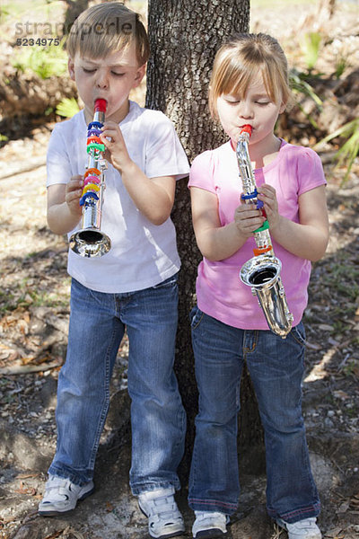 Ein Junge und ein Mädchen stehen an einem Baum und spielen Musikinstrumente.