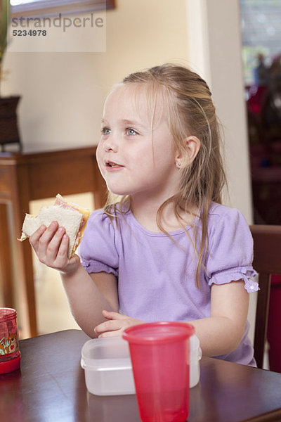 Ein Mädchen  das an einem Tisch sitzt und ein Sandwich isst.