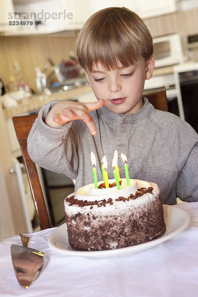 Ein Junge sitzt hinter einem Geburtstagskuchen mit angezündeten Kerzen.
