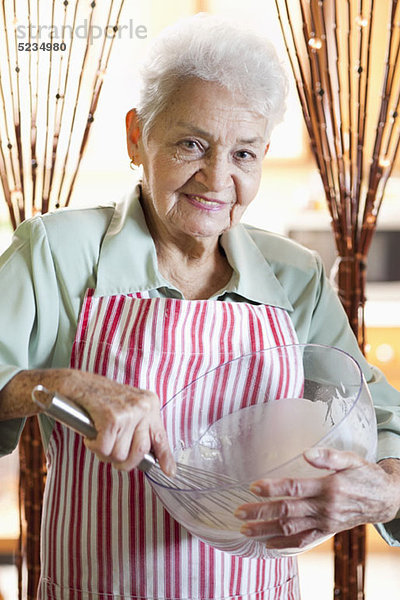 Porträt einer älteren Frau  die Zutaten in einer Schüssel mischt.
