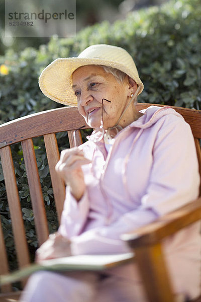 Eine ältere Frau  die draußen auf einer Bank sitzt.