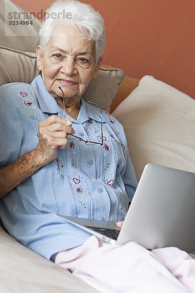 Eine ältere Frau sitzt auf einem Sofa mit einem Laptop.