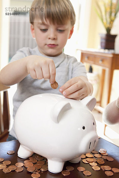 Ein Junge  der Münzen in ein Sparschwein steckt.