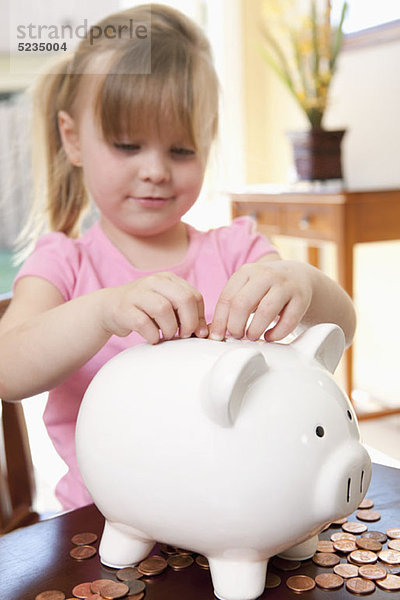 Ein Mädchen  das Münzen in ein Sparschwein steckt.