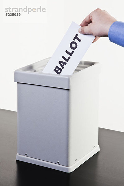 Ein Mann  der ein Papier mit dem Wort BALLOT in eine Wahlurne legt  Hände in Nahaufnahme.