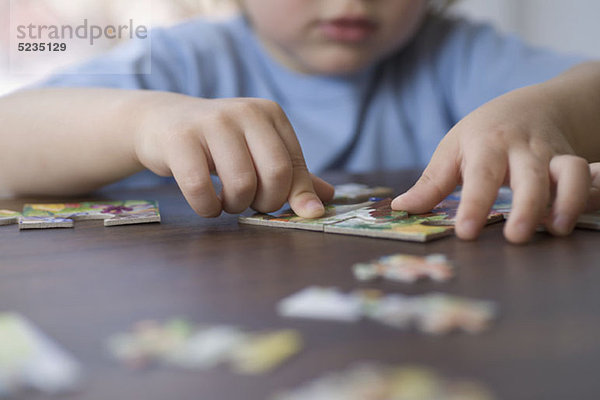 Ein kleiner Junge  der ein Puzzle macht  konzentriert sich auf die Hände.