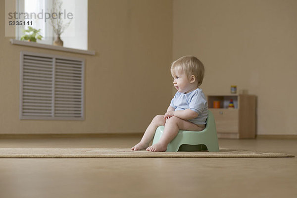 Ein fröhliches Kleinkind sitzt auf einem Töpfchenstuhl und schaut weg.
