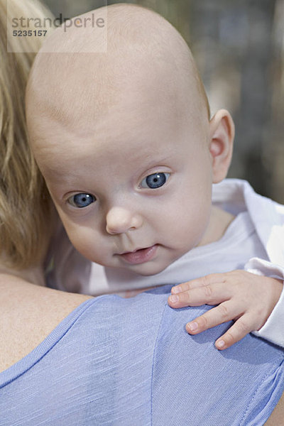 Eine Mutter  die ein Baby hält  über der Schulter  konzentriert sich auf das Gesicht des Babys.