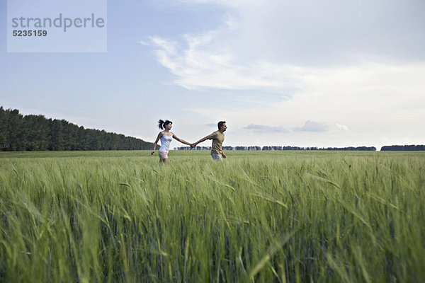 Ein Mann und eine Frau halten sich an den Händen und rennen durch ein Weizenfeld.