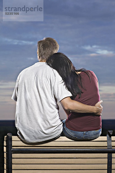 Ein Paar sitzt auf einer Bank und beobachtet den Sonnenuntergang.