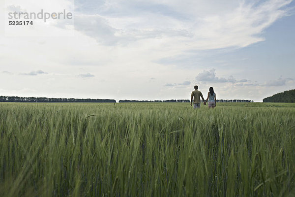 Ein Mann und eine Frau gehen Hand in Hand durch ein abgelegenes Weizenfeld.