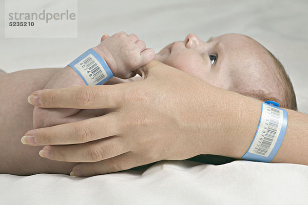 Ein Baby  das den Daumen seiner Mutter hält  beide mit Krankenhausarmbändern.
