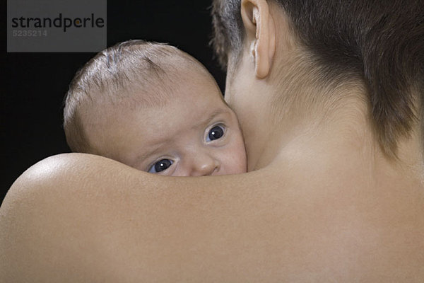 Eine Mutter  die ein Baby hält  über der Schulter  konzentriert sich auf das Gesicht des Babys.