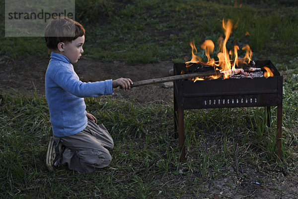 Ein Junge  der ein Feuer in einer Feuerstelle im Freien anstößt.