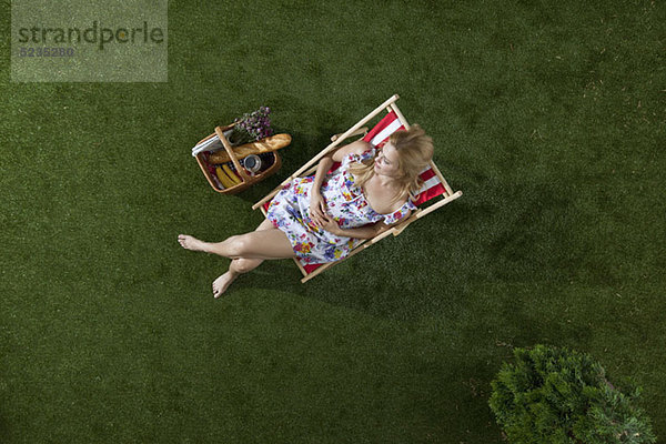 Eine Frau sitzt in der Sonne auf einem Gras in einem Park mit Picknickkorb  Blick nach oben