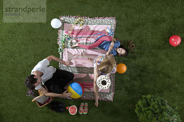 Eine Familie feiert bei einem Picknick im Park mit Kuchen  Luftballons und Luftschlangen  Blick nach oben.