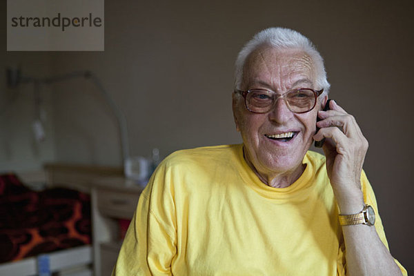 Ein fröhlicher älterer Mann  der in einem Pflegeheim lebt und ein Handy benutzt.
