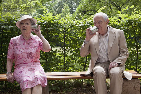 Ältere Männer und Frauen sprechen miteinander auf Blechdosentelefonen auf der Bank im Park.