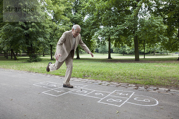 Älterer Mann  der Hopscotch im Park spielt.