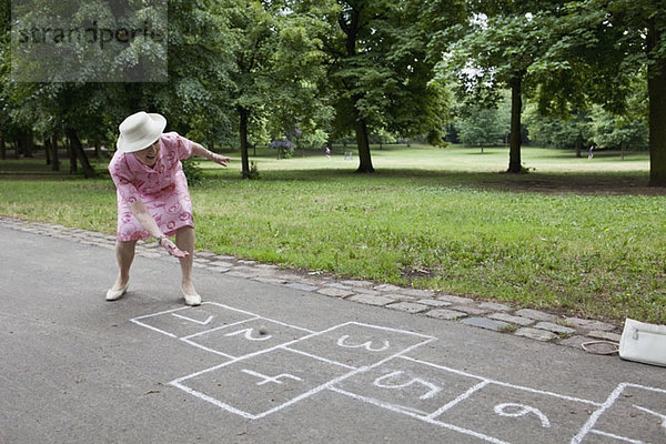 Seniorin rollt einen Stein  während sie Hopscotch spielt.