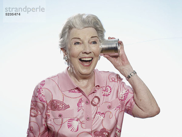 Seniorenfrau hört komisch auf Blechdosentelefon