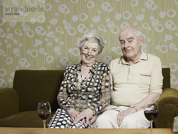 Mann und Frau entspannt auf dem Sofa  mit zwei Gläsern Rotwein auf dem Tisch davor