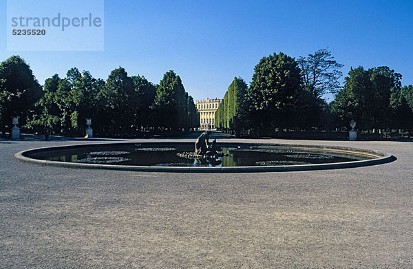 Österreich  Wien  Wasserfontäne mit Schloss Schönbrunn weit im Hintergrund zwischen Bäumen gesehen