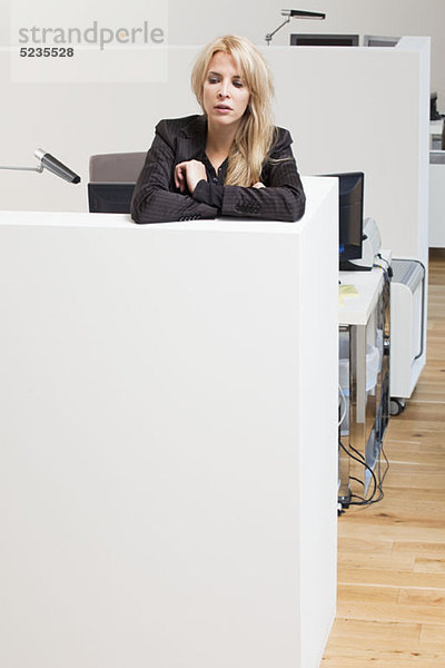Geschäftsfrau  die sich auf eine Bürozelle stützt und nach unten schaut.