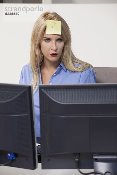 Frau starrt auf den Computer mit Klebezettel auf der Stirn.