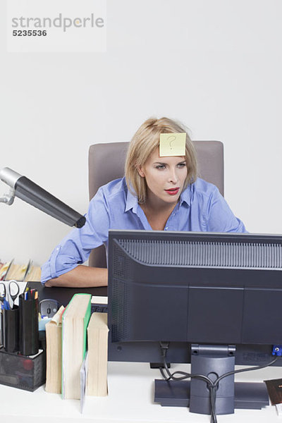 Frau schaut auf den Computer mit einem Klebezettel auf der Stirn.