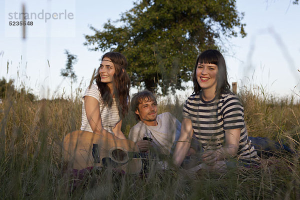 Drei Freunde unter dem Wiesenlieschgras mit Wein und Gitarre