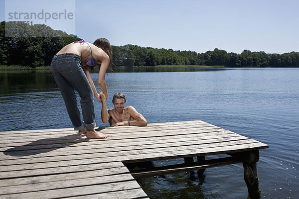 Spaß als Frau hilft dem Mann aus dem Wasser auf dem Steg