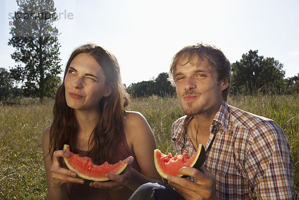 Paar sitzend essende Melone im Feld