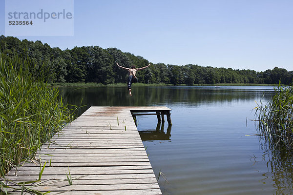 Der Typ am Steg taucht mit ausgestreckten Armen in den See.