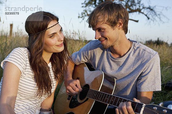 Mann spielt Gitarre für seine Freundin im Feld