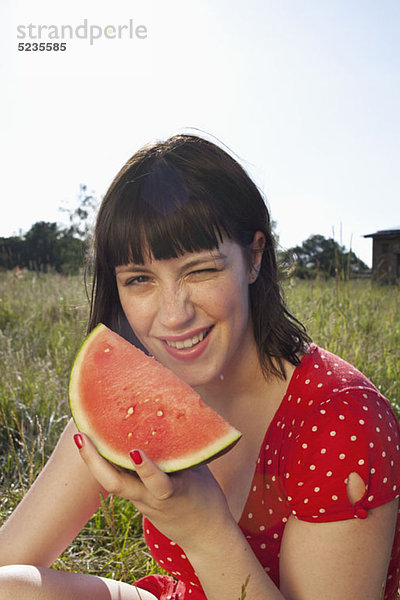 Mädchen im Feld sitzend mit einer Scheibe Melone in der Hand