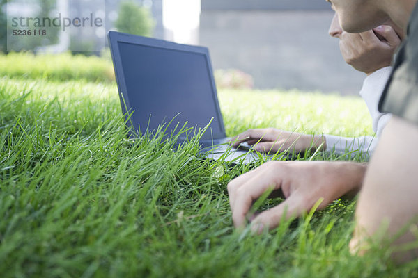Leute  die Laptop-Computer benutzen  während sie auf Gras liegen  beschnitten