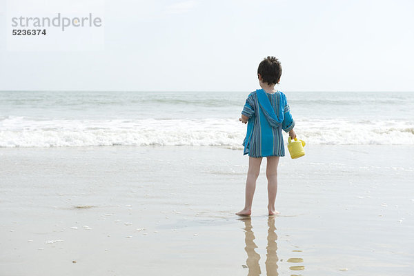 Junge steht am Strand und schaut auf den Ozean.