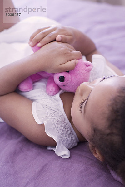 Kleines Mädchen auf dem Bett liegend mit Teddybär