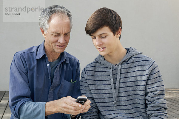 Vater und Sohn benutzen gemeinsam das Handy