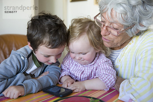 Großmutter und junge Enkelkinder schauen gemeinsam aufs Handy