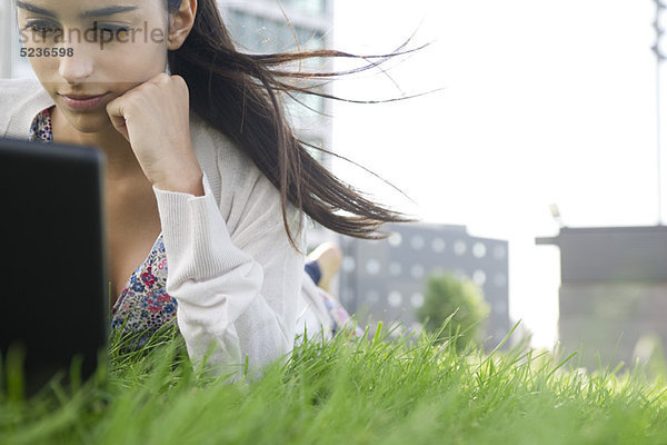 Junge Frau auf dem Bauch liegend auf Gras mit im Wind wehendem Haar