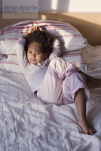 Kleines Mädchen im Pyjama auf dem Bett liegend