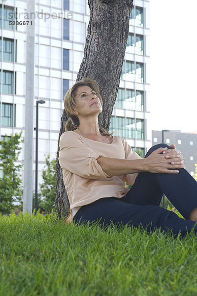 Frau im Gras sitzend  in Gedanken aufschauend