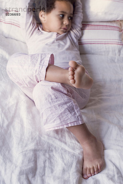 Kleines Mädchen im Pyjama auf dem Bett liegend